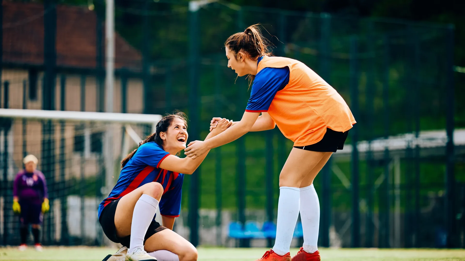 A soccer player helping a teammate up from the field
